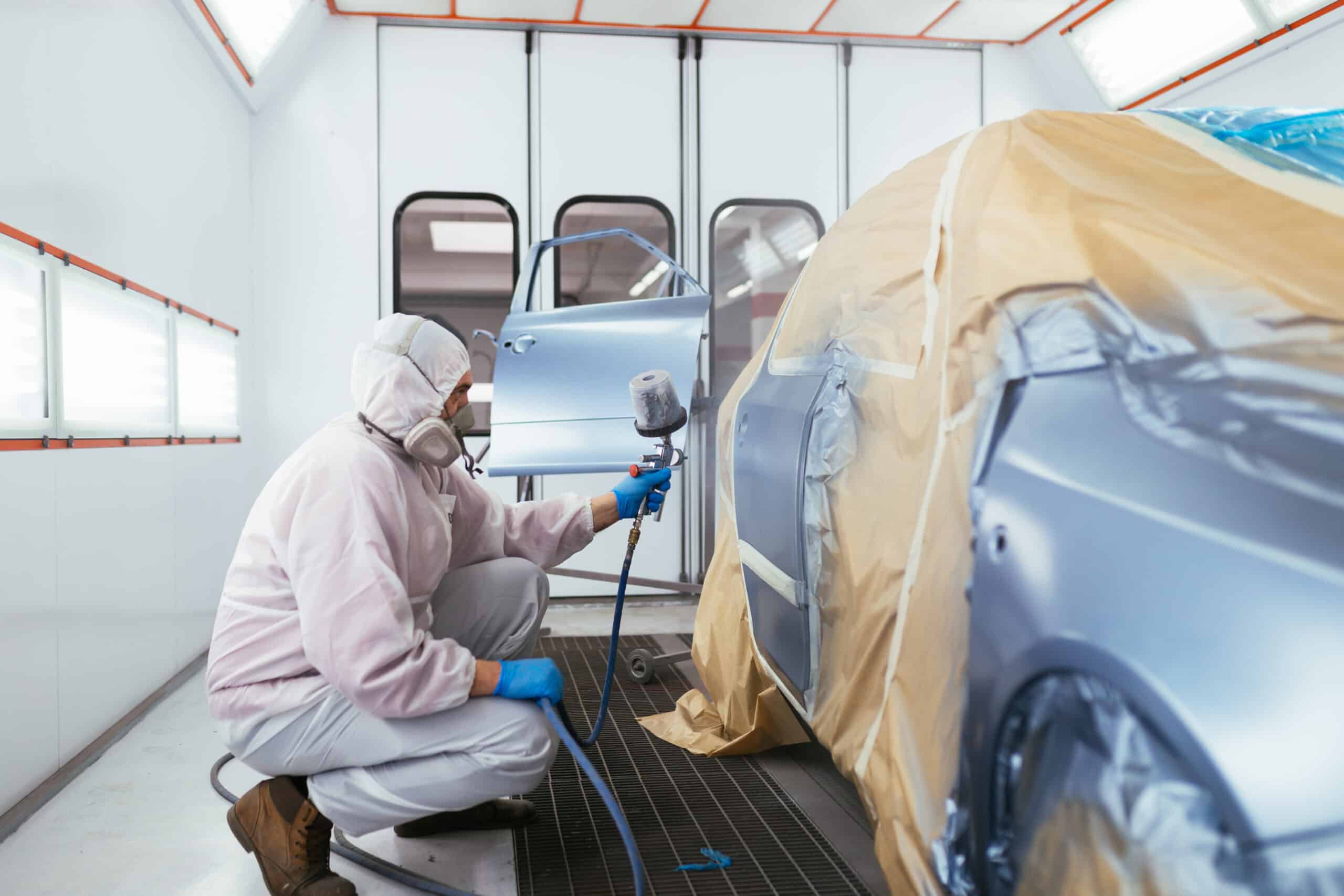 Man with protective clothes and mask painting car using spray compressor.