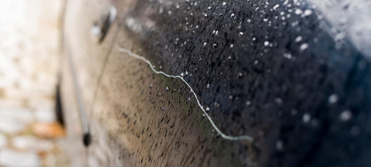 Scratched car paint with door handle and tire out of focus